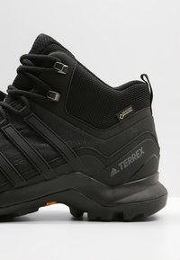 Chaussure de randonnée noire avec une tige synthétique texturée, un système de laçage et une semelle en caoutchouc moulée. Présente le logo Terrex et le marquage Gore-Tex.