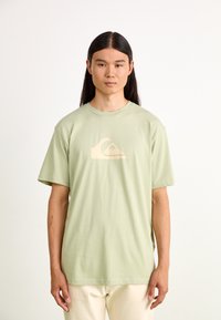 Light green cotton t-shirt with a crew neck and short sleeves, featuring a beige wave logo design on the front.