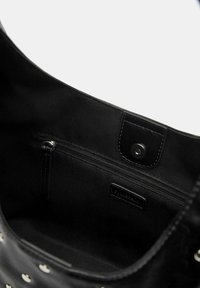 Interieur van zwarte tas met een ritsvak, gladde stofvoering en drukknoopsluiting. Het interieur is ruim en naadloos met minimale designdetails.