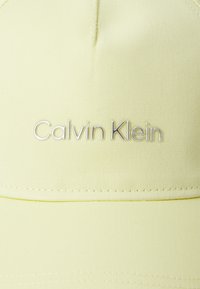 Căciulă galbenă Calvin Klein, realizată dintr-un material texturat, având un logo argintiu brodat pe față și detalii cusute pe margine.