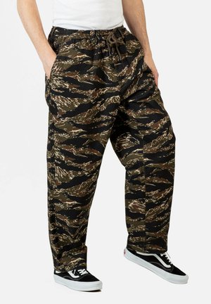 Camo-patterned, elastic-waist pants in dark green, brown, and black. Features side pockets and a relaxed fit. Textured cotton material.