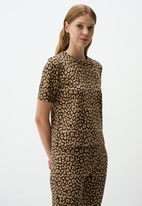 Set van een top en broek met luipaardprint, gemaakt van zachte stof; beschikt over korte mouwen, een ronde halslijn en een losse pasvorm in bruin en beige tinten.