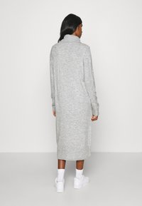 Μακρύ γκρι πλεκτό φόρεμα με ψηλό γιακά,  ribbed μανσέτες και τελείωμα. Το ύφασμα φαίνεται μαλακό με υφή. Φορεμένο με λευκά sneakers.