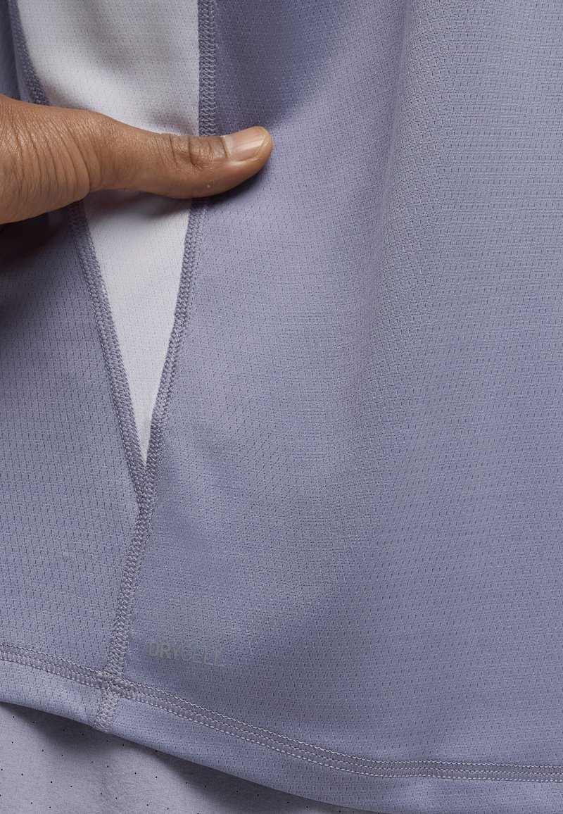 Tissu sportif violet clair avec une texture apparente et une technologie d'évacuation de l'humidité. Comprend une couture centrale et une étiquette avec logo.