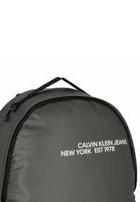 Zaino in nylon nero dalla forma arrotondata, con la scritta bianca "CALVIN KLEIN JEANS NEW YORK EST 1978" e una robusta maniglia superiore.