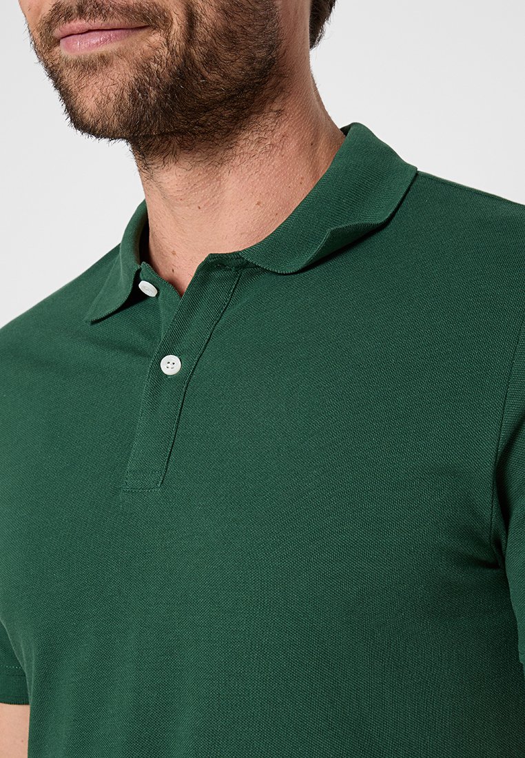 Polo vert en tissu texturé, avec un col rabattu, deux boutons blancs et des manches courtes. Pas de motifs ou graphiques visibles.