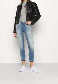 Svart läderjacka, grå polotröja med rosbroderi, blekta blå slim-fit jeans och vita sneakers. Ren design med avslappnad passform.