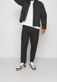 Svart vadderad jacka, vit t-shirt, svarta upptill smalnande byxor och svarta sneakers med röda och vita accenter. Enkelt design med funktionella fickor.