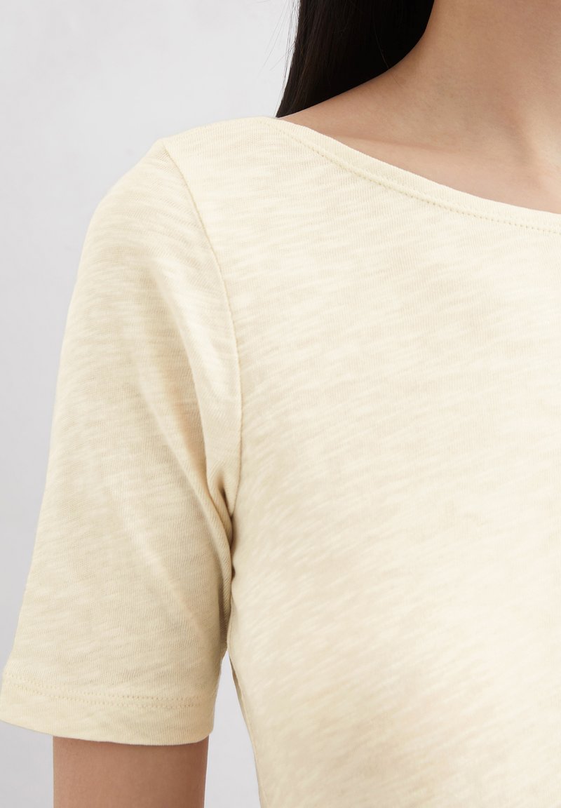 Kurzarmpullover in hellem Beige mit einem weichen, strukturierten Stoff und einem weiten Ausschnitt. Nahtdetails sind an den Schultern sichtbar.