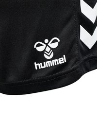Svarta sportshorts tillverkade av ett tyg med en slät textur, med en vit Hummel-logotyp och diagonala chevron-mönster på sidan.