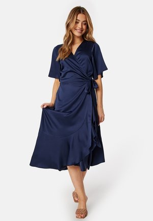 Robe portefeuille en satin bleu marine avec des manches courtes, une taille cintrée, et une silhouette fluide, présentant un ourlet superposé et une texture lisse.