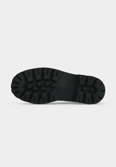 Semelle de bottes noire avec des crampons profonds et robustes conçus pour une forte adhérence et une durabilité sur des surfaces rugueuses.