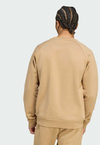 Sudadera beige con cuello redondo acanalado y mangas largas, que presenta una textura suave y un ajustado relajado. La vista trasera no muestra gráficos.