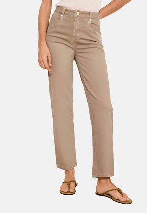 Person wearing high-waist, straight-leg beige pants paired with brown sandals, standing against a plain light background.