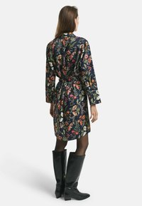 Blaues Kleid mit Blumenmuster, langen Ärmeln und Taillengürtel, aus leichtem Stoff. Kombiniert mit knielangen schwarzen Stiefeln.