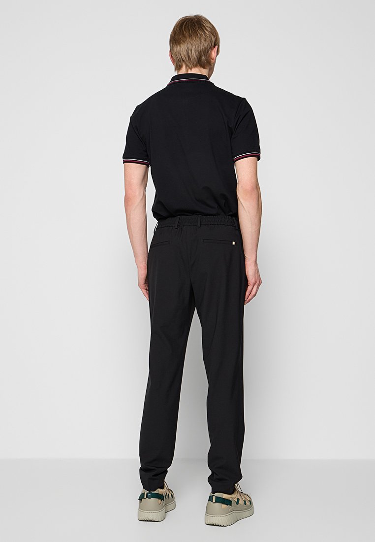 Polo noir avec un col contrasté et un pantalon noir slim-fit, doté d'une taille élastique et de poches arrière. Chaussures de couleur neutre.