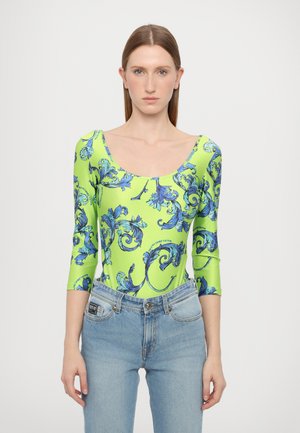 Body a maniche lunghe di colore verde chiaro con un motivo a vortice floreale blu, dotato di scollatura a barco e silhouette aderente. Abbinato a jeans chiari.