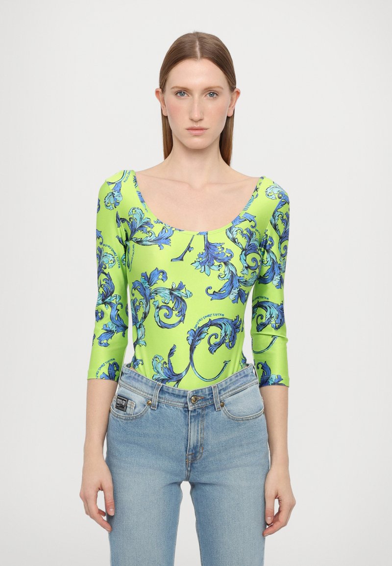 Langermet bodysuit i lys grønn med blå blomsterwiral mønster, med en scoop-hals og en tettsittende silhuett. Kombinert med lyse jeans.