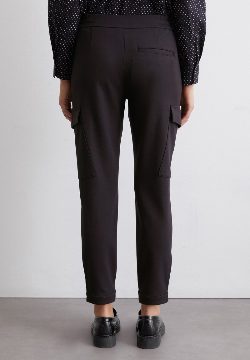 Czarne spodnie cargo z elastycznego materiału, długości do kostek, z bocznymi kieszeniami. Gładka faktura, minimalne detale, noszone z czarnymi butami.