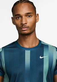 Μπλούζα Nike κοντομάν�ικη σε σκούρο μπλε και τιρκουάζ, με γεωμετρικά σχέδια, λαιμόκοψη crew και μικρό λευκό λογότυπο Nike στο στήθος.