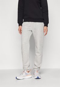 Graue Sweatpants aus weichem Material, mit einem elastischen Bund und tapering Beinen, kombiniert mit leichten Sportschuhen. Schwarzes Rundhals-Sweatshirt.