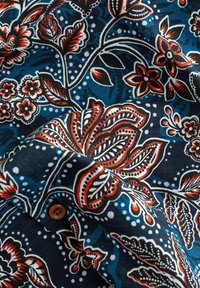 Baumwollgewebe mit einem dunkelblauen Hintergrund und roten sowie weißen Blumenmustern, kunstvollen Details und einem braunen Knopfakzent.