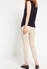 Granatowy bezrękawnik w połączeniu z jasnobeżowymi spodniami typu tapered. Stylizacja charakteryzuje się gładką fakturą i jest uzupełniona ciemnym obuwiem.