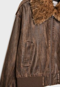 Giacca marrone in finta pelle con colletto in pelliccia sintetica, chiusura frontale con zip, tasche laterali e orlo a coste. La texture invecchiata arricchisce il design.
