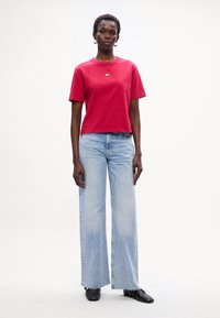 Rød t-shirt med korte ærmer og rund hals, parret med lyseblå vide jeans. Sorte sko fuldender outfittet.