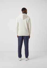 Sweatshirt creme com cordão, combinado com calças de treino azul-marinho com punhos com fecho e detalhes refletivos. Ténis brancos completam o visual.