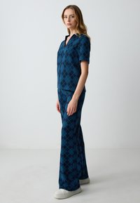 Outfit argyle blu e teal con top a maniche corte e scollatura a V, accompagnato da pantaloni svasati, realizzato in tessuto morbido e testurizzato.