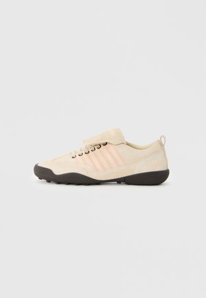 Beige ruskinds sneakers med rosa side-striber, rund tå og sort tekstureret sål. Har en blød tunge og hæl-loop med prægede tallet "1964."