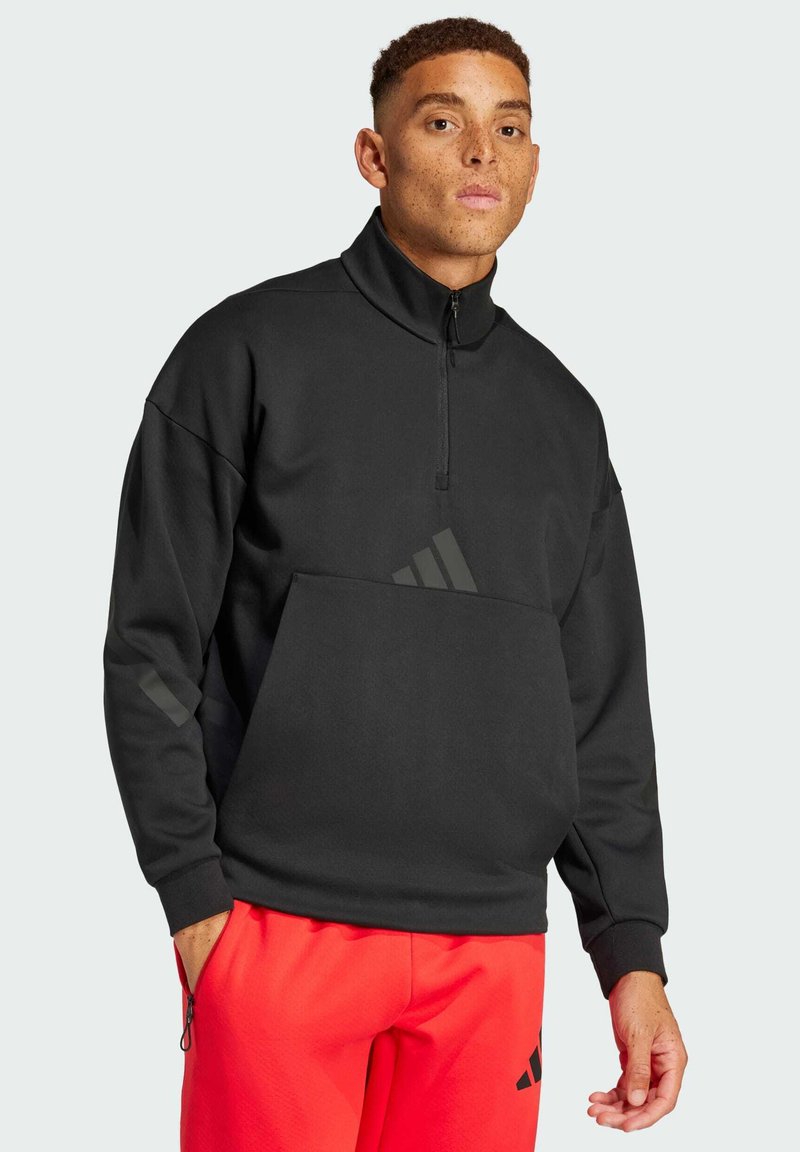 Svart zip-up sweatshirt med hög krage, framficka och diskret logodetalj. Bärs med röda sweatpants. Slät textur, avslappnad passform.