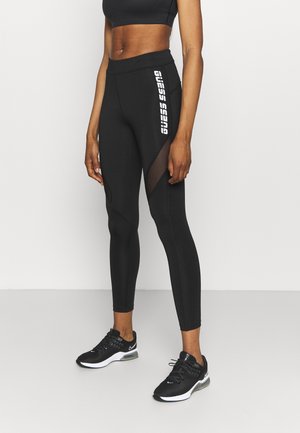 Leggings noirs avec des panneaux en mesh et un logo blanc sur le côté. Tissu lisse et extensible, conception ajustée et ourlet à la cheville.