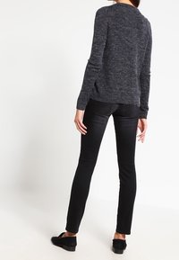 Donkergrijze gebreide trui met lange mouwen, ronde hals en gestructureerde afwerking. Gecombineerd met zwarte slim-fit jeans en zwarte platte schoenen.