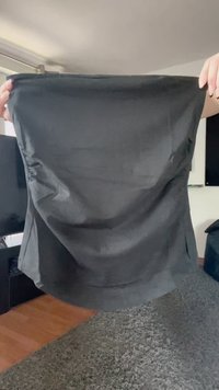 Ruke drže rastegnutu crnu tkaninu ili materijal unutra, iznad tepih podnice, s namještajem u pozadini.