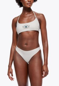 Set bikini grigio chiaro composto da un reggiseno a triangolo con motivo decorativo di occhi e strass, abbinato a culotte a vita bassa.