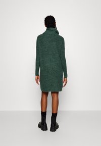 Grön stickad klänning med hög krage, långa ärmar och en avslappnad passform. Texturen är mjuk med en lätt fluffig yta.