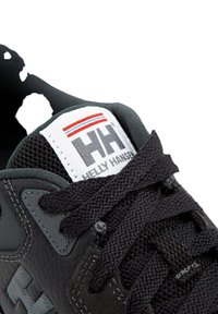 Černé tenisky s texturovaným koženým svrškem, síťovaným jazykem a černými tkaničkami. Mají bílou nášivku s červenými a modrými pruhy.