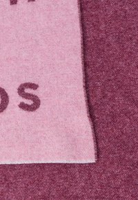 Világos rózsaszín textil sál sötét rózsaszín tipográfiával. Puha textúra, rojtos szegélyekkel és kontrasztos, sötétebb mályva hátterű.