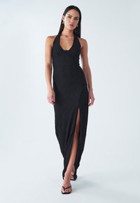 Svart maxiklänning med halterneck, texturerat tyg, sidospalt och figurnära siluett. Bärs med svarta remsandaler.
