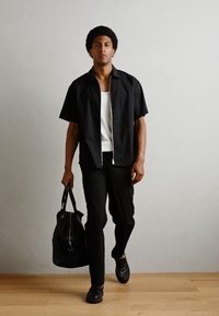 Svart t-skjorte med kort erme og glidelås, hvit tanktop, svarte bukser og svarte lærresorter; bærer en stor svart lærveske.