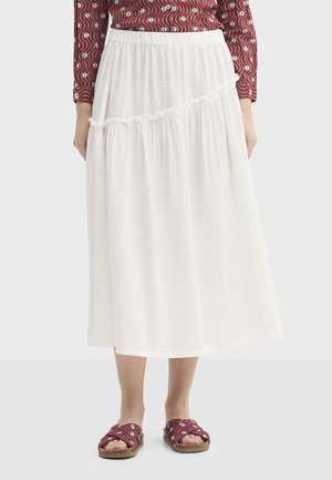 White midi skirt with textured fabric, features layered ruffles along the hem and an elastic waistband. Completed with patterned sandals.