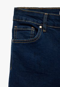 Donkerblauwe denim jeans met oranje stiksel, een voorzak en een knoopsluiting. Glad textuur en op maat gemaakt ontwerp.