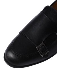 Scarpa in pelle nera dal design elegante, con punta cucita, una larga fascia e una fibbia in tono argento. Texture liscia su tutta la superficie.