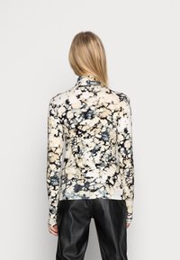 Lange mouwen, vormgevend top van een zachte stof, met een spetterpatroon in crème, zwart en blauwe tinten, met een hoge kraag.