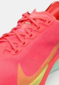 Felroze sportieve schoen met een gestructureerde bovenkant, contrasterende veters en een groen en gele zool. Bevat een ribbelontwerp en merkdetails.