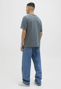 Camiseta de algodón gris con mangas cortas, combinada con jeans azules sueltos que tienen bolsillos traseros y un lavado ligero. Diseño simple, sin patrones.