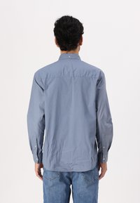 Cămașă bărbătească cu mânecă lungă, albastru deschis, guler cu nasturi, detaliu la cusătura din spate, material din bumbac moale, manșete cu închidere prin nasturi.