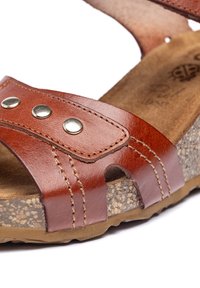 Bruine leren sandaal met twee verstelbare banden met metalen studs, een gestructureerde binnenzool en een kurkachtige zool.